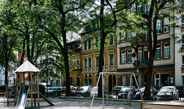 Ein Spielplatz mit Bäumen und parkenden Autos im Hintergrund